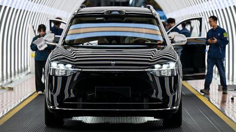 Employees inspects a shiny black Seres electric sports utility vehicle in a production line at factory in China