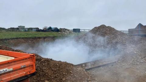 Smoke rising from a hole in the ground with small mounds of rubble on either side