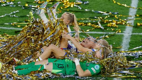 Four footballers from England's Euros winning squad lie on the pitch covered in shiny gold and silver streamers.