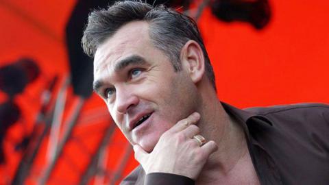 Morrissey wearing a black shirt in front of a red background