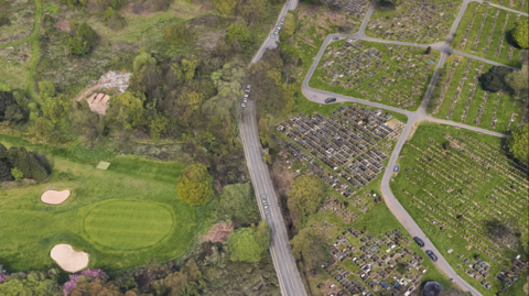 An ariel shot showing a carriageway, parked cars on a field and golf course.
