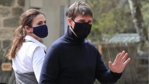 Tom Cruise and co-star Hayley Atwell are pictured filming Mission Impossible in North Yorkshire. It was during Covid so both are wearing masks. Cruise is wearing a blue polo neck jumper and is waving to onlookers.