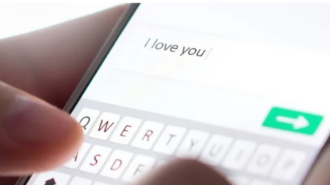 A person hold a phone in their hands with a message on screen that says 'I love you'. The image is close up.