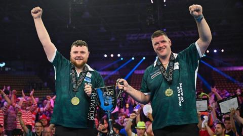 Josh Rock and Daryl Gurney holding the World Cup of Darts trophy