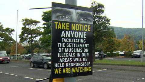 A poster that reads 'Take notice anyone facilitating the settlement of Muslims or illegals in our areas will be held responsible. We are watching' it also has a picture of a persons eyes along the top of the poster.