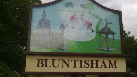 Bluntisham village sign - showing skaters and a church