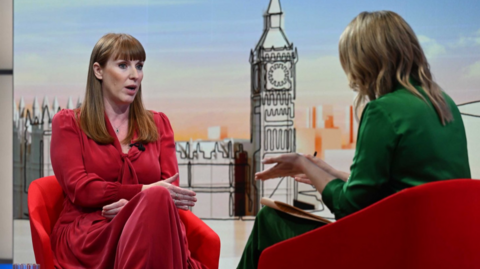 Angela Rayner in red dress sitting down in a red chair as she answers questions to Laura Kuenssberg (R) in a green suit sitting opposite her