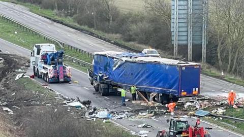 Recovery work is under way after a lorry has had a collision on the A1 in Lincolnshire in March.  There are men in hi-vis suits clearing the road of a substantial amount of debris. There is a badly damaged lorry in the photo.