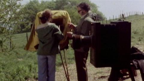 Two people standing outside, looking at some large vintage cameras.