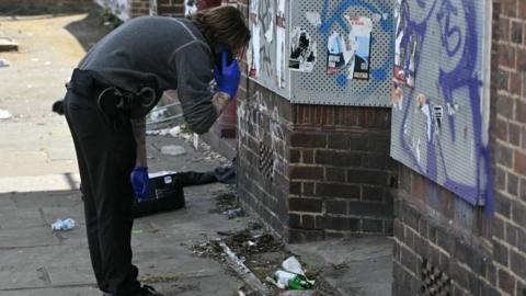 A policeman looks at a glass bottle outside a building