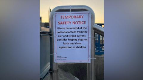 A laminated paper signage attached to a ramp reads TEMPORARY SAFETY NOTICE and advises people to be mindful of potential falls and keep dogs on leads. 