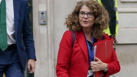 Policing minister Diana Johnson leaves the Cabinet Office in Westminster, central London wearing a red coat.