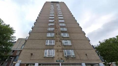 A photo from the ground looking up at Combe House, a nondescript 70s style high-rise residential building. There are more modern high-rise buildings and trees in the background. 