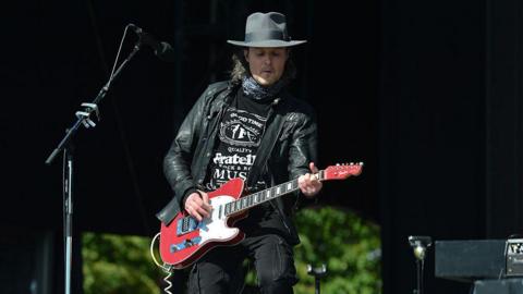 Jon Fratelli onstage - he is playing guitar, wearing a black hat, black T-shirt and leather jacket