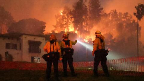 Firefighters operate as smoke and flames rise from the Sunset Fire in the hills overlooking the Hollywood neighborhood of Los Angeles, California