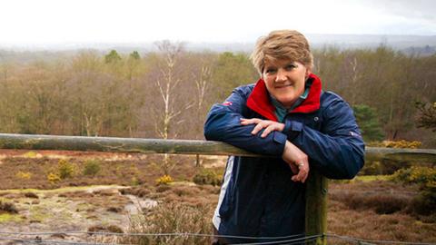 Clare Balding outside leaning on a wooden fence.