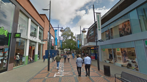 The Parade in Swindon. Shops can be seen either side of the street, as well as benches, flags and people. 