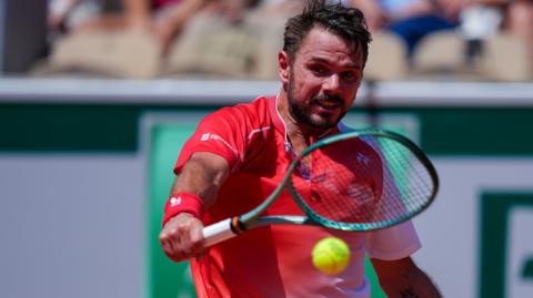Stan Wawrinka hits a backhand wearing a red and white shirt