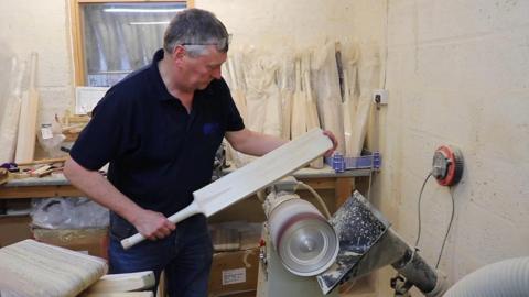 Martin Berrill holding a wooden cricket bat in his workshop