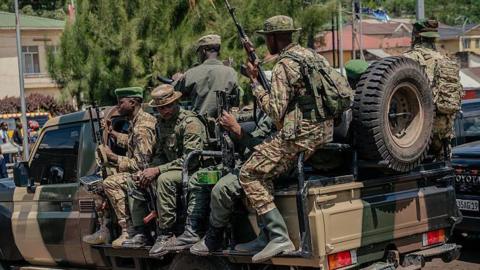 Soldiers in uniform, with guns, atop a pickup truck