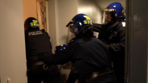 Uniformed police force entry to a flat in a block of tenements