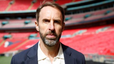 Gareth Southgate has a neutral expression in a picture posed in a football stadium.