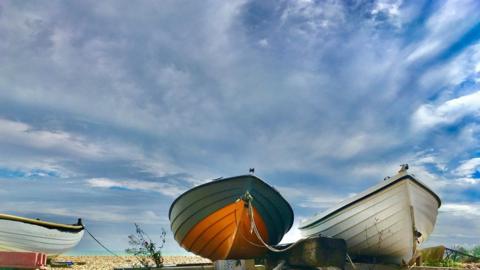 Small rowing boats on a beach with cloudy blue sky behind