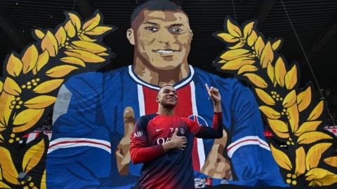 Kylian Mbappe in front of a tifo banner displayed by PSG fans
