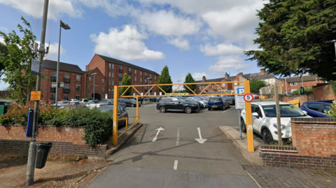 Entrance to a car park with a block of flats in the background