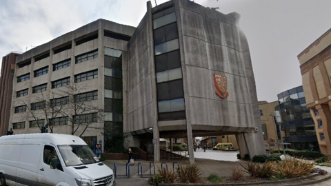 A grey concrete building with a red crest on the side of it.