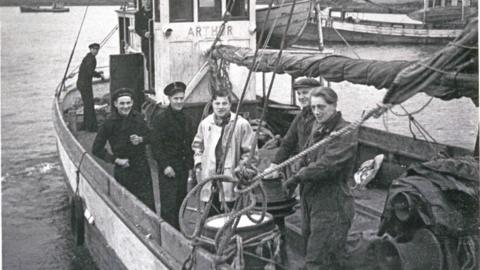 A black-and-white image of men on a fishing boat looking at the camera.