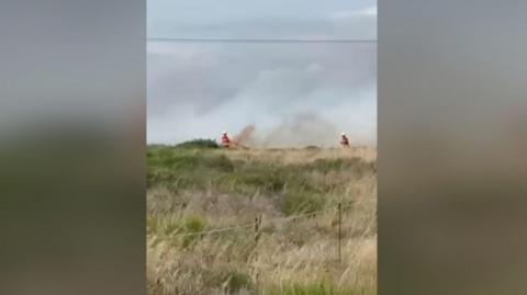 Fire crews in a field in Romney Marsh using high pressure hoses to put out flames