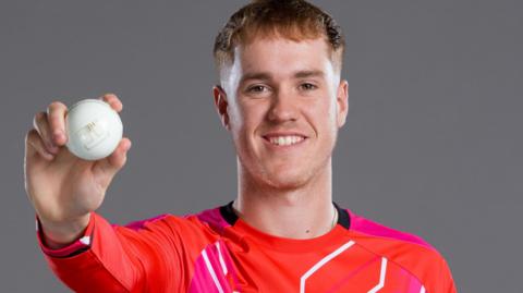 Ben Kellaway holding a cricket ball in a Welsh Fire shirt