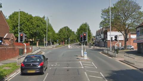 The junction of Stainbeck Road and Stainbeck Avenue. A car has stopped at the traffic lights which are on red.