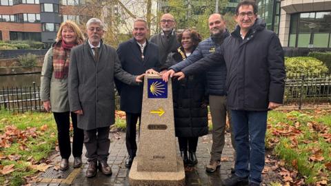 A group of seven people standing next to the granite marker.