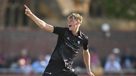Alfie Ogborne holds one arm in the air in celebration after taking a wicket