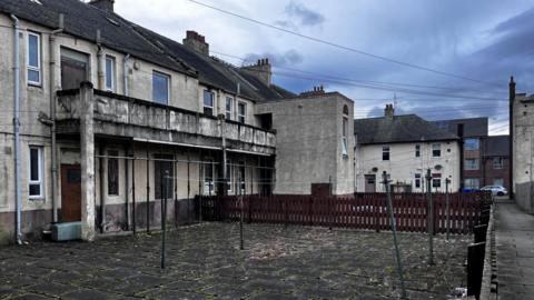 Two storey flats with a flagstone courtyard, washing line and telephone cables.