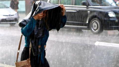 A woman holds her jacket over her head as rain pours down in London