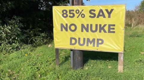 A sign placed on a grass verge that reads '85% say no nuke dump'.