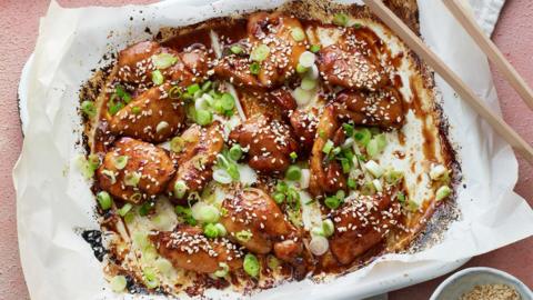 Asian inspired sticky chicken bites in a brown glossy sauce, covered in sesame seeds and spring onions.