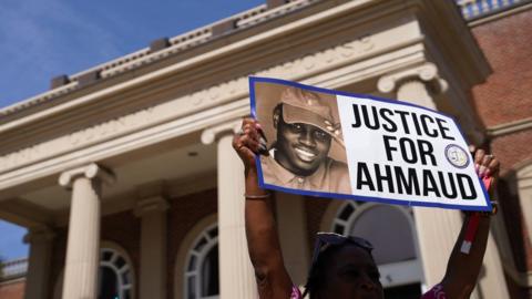 A demonstrator holds a sign at the Glynn County Courthouse as jury selection begins in the trial of the shooting death of Ahmaud Arbery