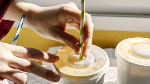 A person puts a straw into a the lid of a takeaway cup