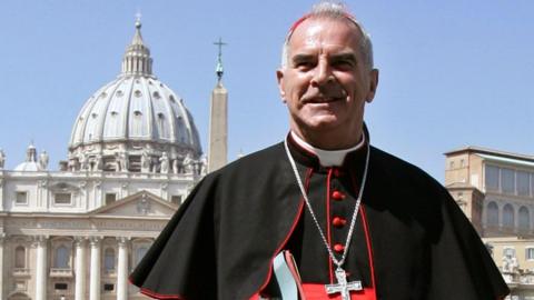 Cardinal Keith O'Brien wearing cassock and with silver crucifix standing in St Peter's Square in Rome with St Peter's dome in the background
