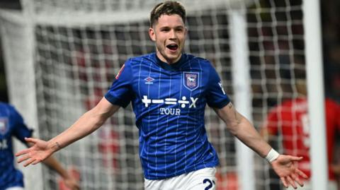 A mid shot of George Hirst. He has short brown hair and is wearing Ipswich Town's Blue pin-striped shirt. 