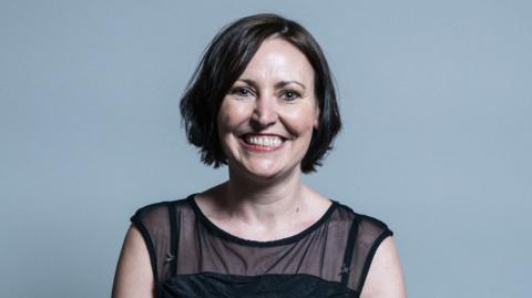 Vicky Foxcroft in her official portrait, smiling at the camera and wearing a dark top. She has short brown hair. 