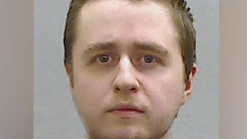 Alexander McCartney's mug shot. He has short brown hair with a bit of stubble on his cheeks and chin and looking directly at the camera.