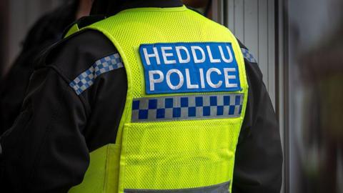 The back of a police officer's high vis jacket which has the words "Heddlu" and "police" written on it 