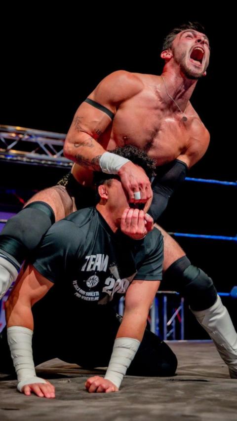 Two wrestlers engaged in combat in the ring. One has his hands in the other's mouth and is screaming at the crowd