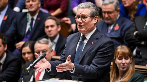 Keir Starmer gestures while speaking in the House of Commons during PMQs, with MPs behind him in view