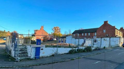 The site of a demolished factory in Ringstead, showing large metal fencing around piles of bricks